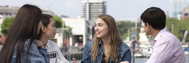 A group of students of different races and genders, sitting and talking at Bristol Harbourside.